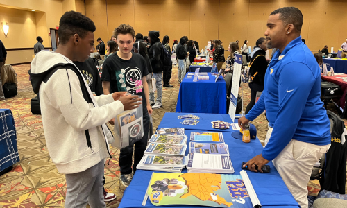  Male student talk with a admissions representative at a college fair.